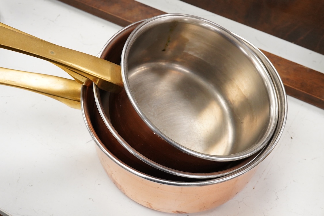 A graduated set of 5 copper brass handled sauce pans and a copper embossed and mahogany hanging rack
